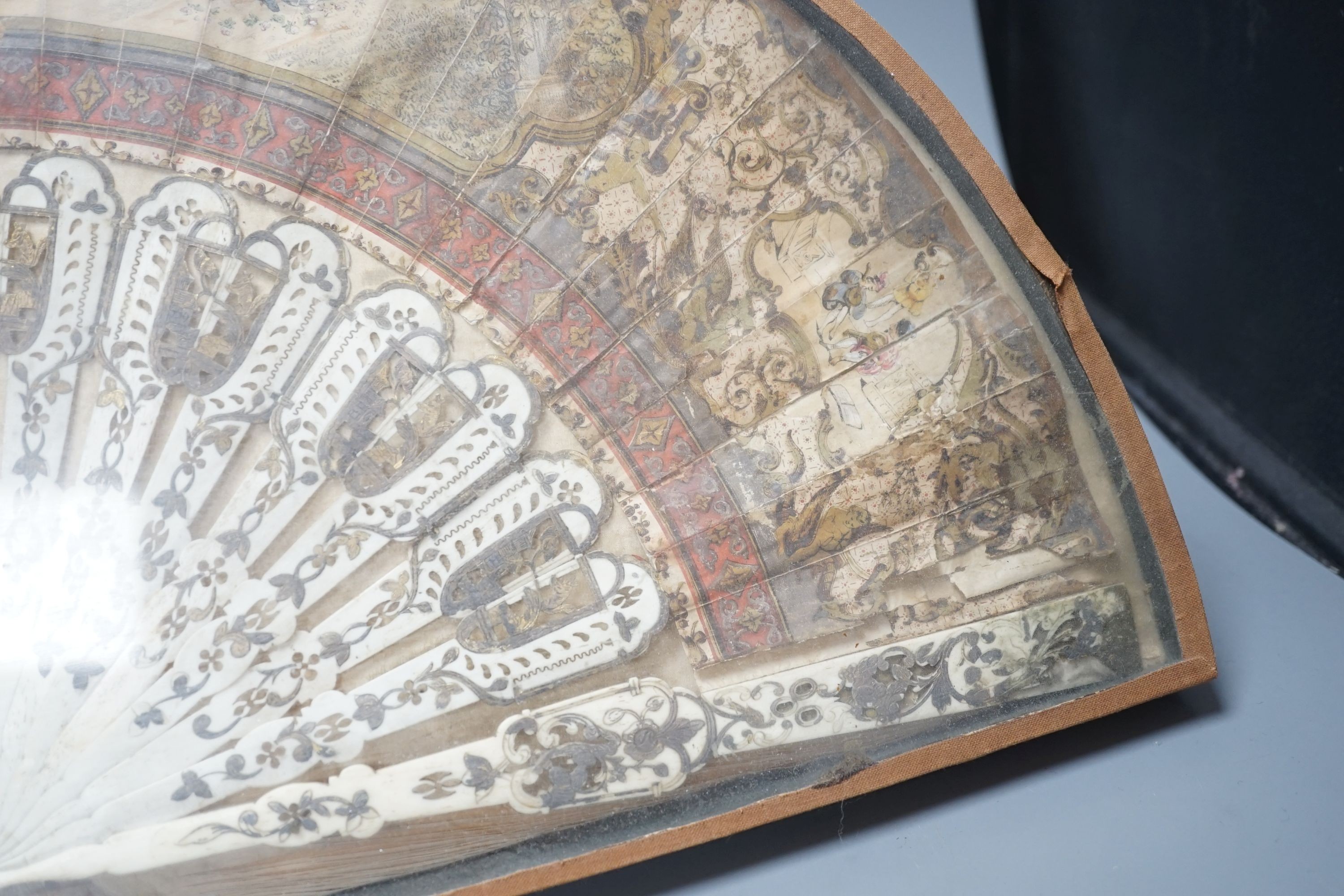 A cased 19th century French lithograph paper leaf and bone stick fan, 56 cms wide.